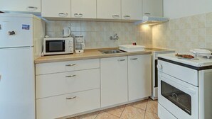 A compact kitchen with white cabinets, a microwave, a coffee maker, and a stove. - Apartment in Senj with Sea Views & BBQ (Senj)