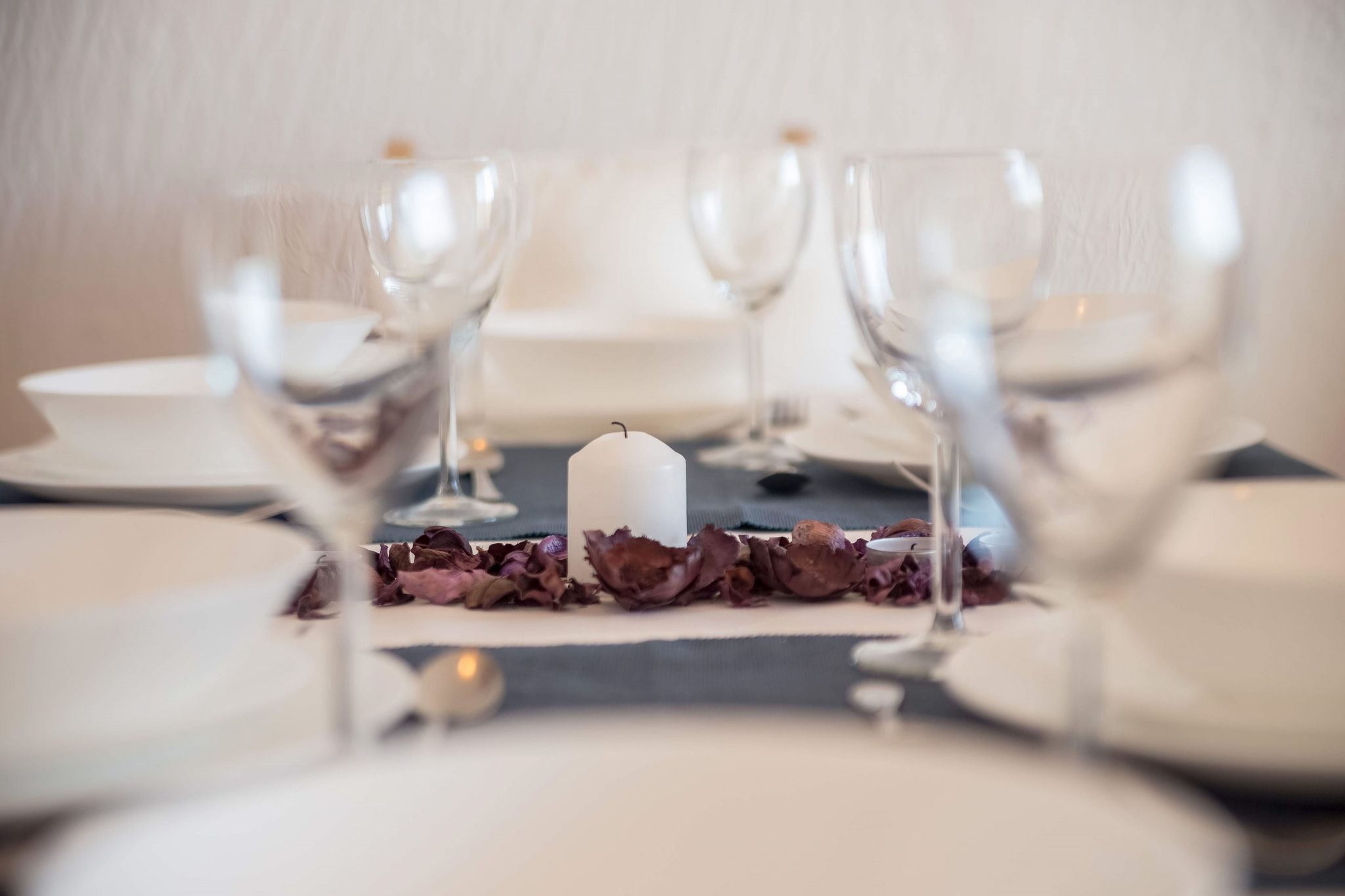 Mesa de comedor dispuesta con platos blancos, copas de vino transparentes y un centro de mesa con una vela blanca.