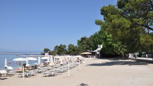 Une plage avec des transats et des parasols, un ciel dégagé et des arbres en arrière-plan.