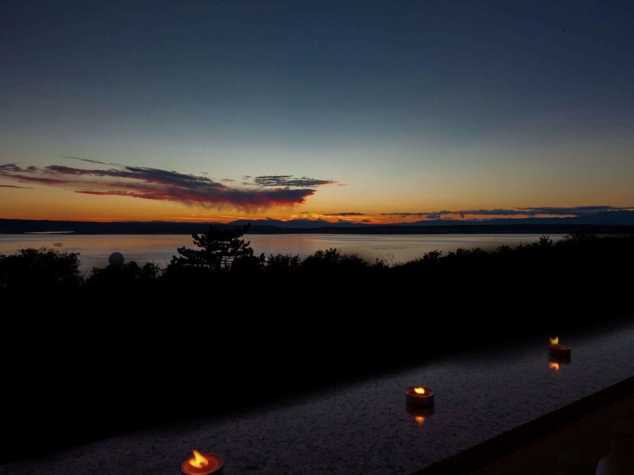 A sunset view over a calm body of water with silhouettes of trees and three lit candles on a ledge.