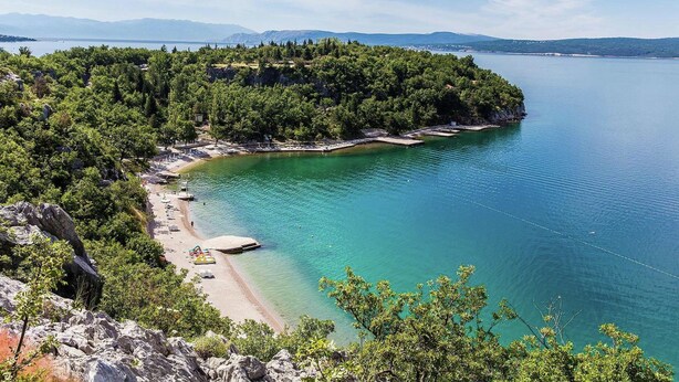 Eine Küstenlandschaft mit Strand, klarem Wasser und einem bewaldeten Gebiet.