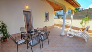 Eine überdachte Terrasse mit Esstisch und Stühlen, umgeben von einer Lounge-Ecke mit einer Bank.