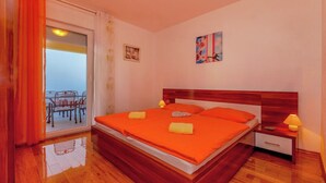 Ein Schlafzimmer mit einem hölzernen Bett, orangefarbener Bettwäsche, einem Nachttisch mit Lampe und Meerblick durch eine Schiebetür.