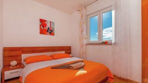 Un dormitorio con cabecera de madera, colcha naranja, una sola obra de arte en la pared y una ventana con vista al cielo.