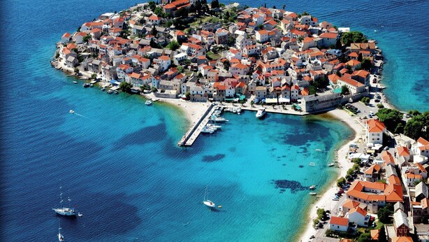 An aerial view of a coastal town with a central pier, surrounded by buildings with red roofs, and boats in the water. - Apartment by the Beach in Dalmatia (Šibenik)