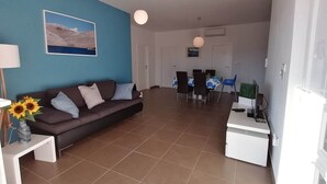 A living room with a brown sofa, a dining table with chairs, and a kitchen area with a white countertop. - Apartment by the Beach in Dalmatia (Šibenik)