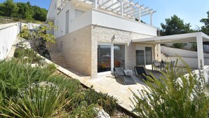 A modern house with a stone facade, a balcony with white railings, and a patio area with outdoor furniture. - Apartment by the Beach in Dalmatia (Šibenik)