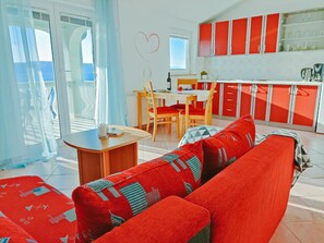 Una sala moderna con un sofá rojo, una mesa de comedor con sillas y una cocina con armarios rojos.