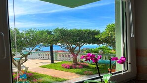Une vue depuis une fenêtre donnant sur un jardin agrémenté d’une fontaine, d’une statue et d’un ciel dégagé.