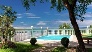 Une piscine bordée d’une balustrade blanche, entourée de verdure et surplombée par un ciel dégagé.