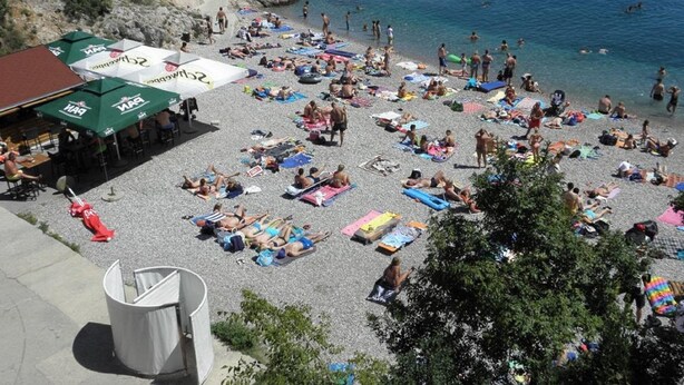 Une plage bondée où les gens se prélassent au soleil et se baignent.