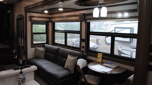 Een gezellig RV-interieur met een leren bank, een klein tafeltje en grote ramen met uitzicht op de omgeving.