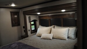 Een slaapkamer met een bed, kussens, een raam en een deur.