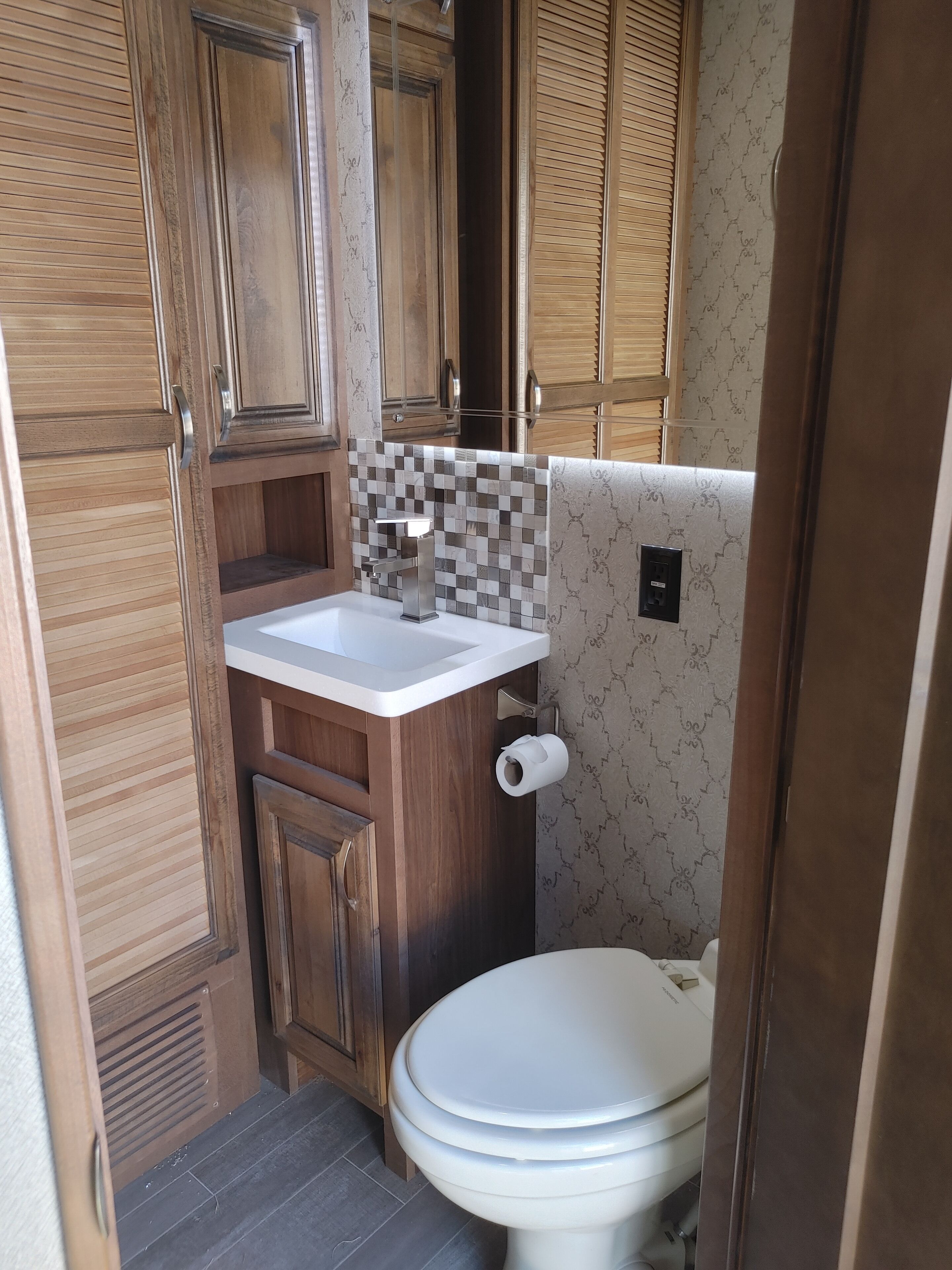 A compact bathroom with wooden cabinets, a white sink, and a toilet.