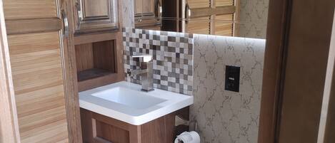 A compact bathroom with wooden cabinets, a white sink, and a toilet.