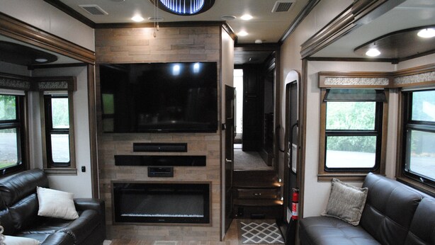 Een modern interieur van een camper met een grote flatscreen-tv, leren banken, een haardvuur en grote ramen.