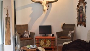 Un salon avec deux fauteuils en osier, un téléviseur et un crâne de taureau accroché au mur.