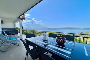 A balcony with a table, chairs, and a view of the sea.
