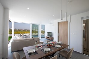 A modern dining area with a large table set for four, a sofa, and a television in the background. - Villa Belle, Brand New Luxury 3BDR Protaras Villa with Private Pool (Protaras)