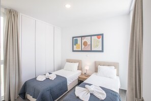 A hotel room with two beds, a nightstand, a wall-mounted artwork, and a window with curtains. - Villa Belle, Brand New Luxury 3BDR Protaras Villa with Private Pool (Protaras)