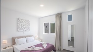 Ett modernt hotellrum med en stor säng, ett nattduksbord, ett konstverk som hänger på väggen, ett fönster med gardiner och en spegel.