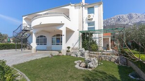 Una casa moderna de dos pisos con fachada curva, un balcón y un camino de piedra que conduce a la entrada.