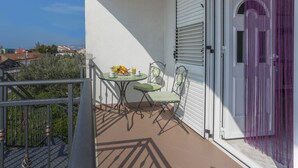 Un balcón con una mesa y sillas, una ventana con persianas y una puerta con cortina púrpura.