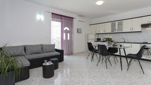 Una sala moderna con un sofá seccional gris, una mesa de comedor con cuatro sillas y una zona de cocina con armarios blancos y un microondas.