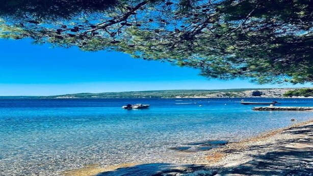 Une vue dégagée sur la côte, avec des eaux calmes, une plage de galets et des îles rocheuses à l’horizon.