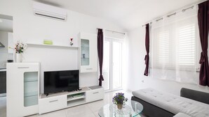 Un salon moderne doté d’un téléviseur à écran plat, d’une table basse en verre, d’un canapé et d’une porte-fenêtre coulissante donnant sur un balcon.
