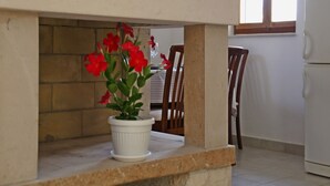 A potted plant with red flowers on a stone ledge in a kitchen area with wooden chairs and a white refrigerator. - Holiday Home in Lumbarda with Garden (Lumbarda)