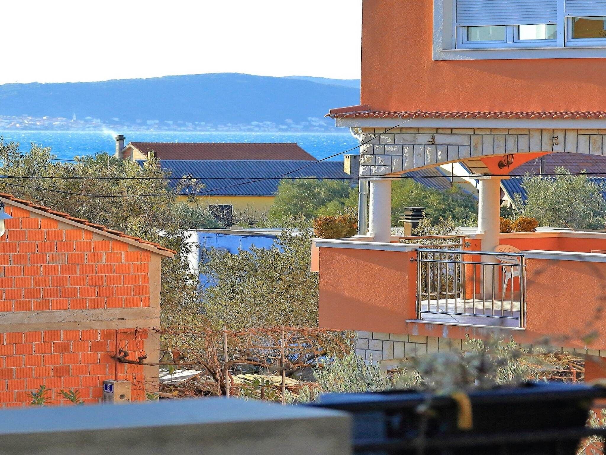 A residential building with a red brick facade, a balcony with a metal railing, and a view of a blue swimming pool and distant mountains.