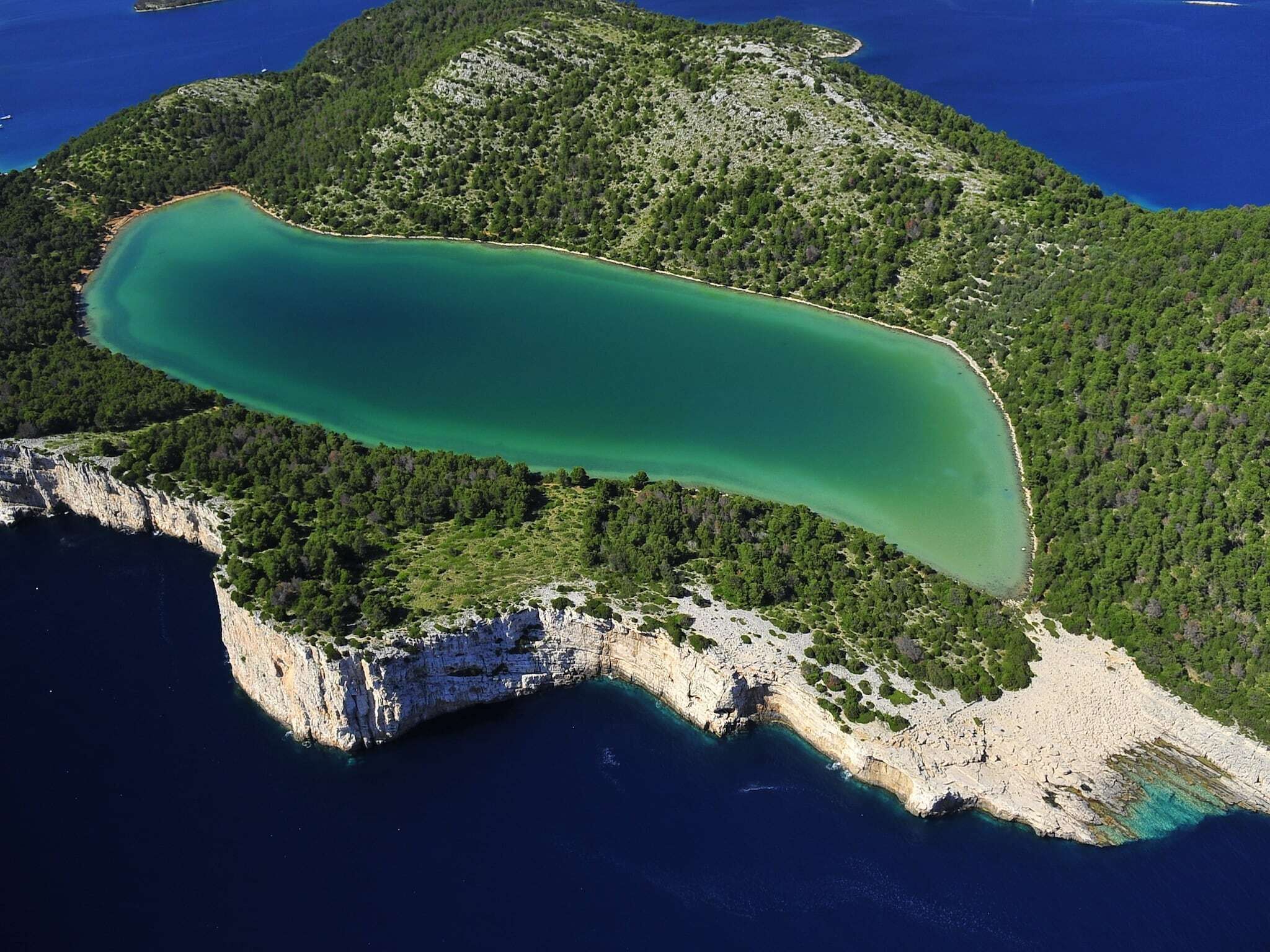 Une vue aérienne d’une zone côtière, avec une étendue d’eau importante et allongée, bordée de collines boisées et de falaises rocheuses.