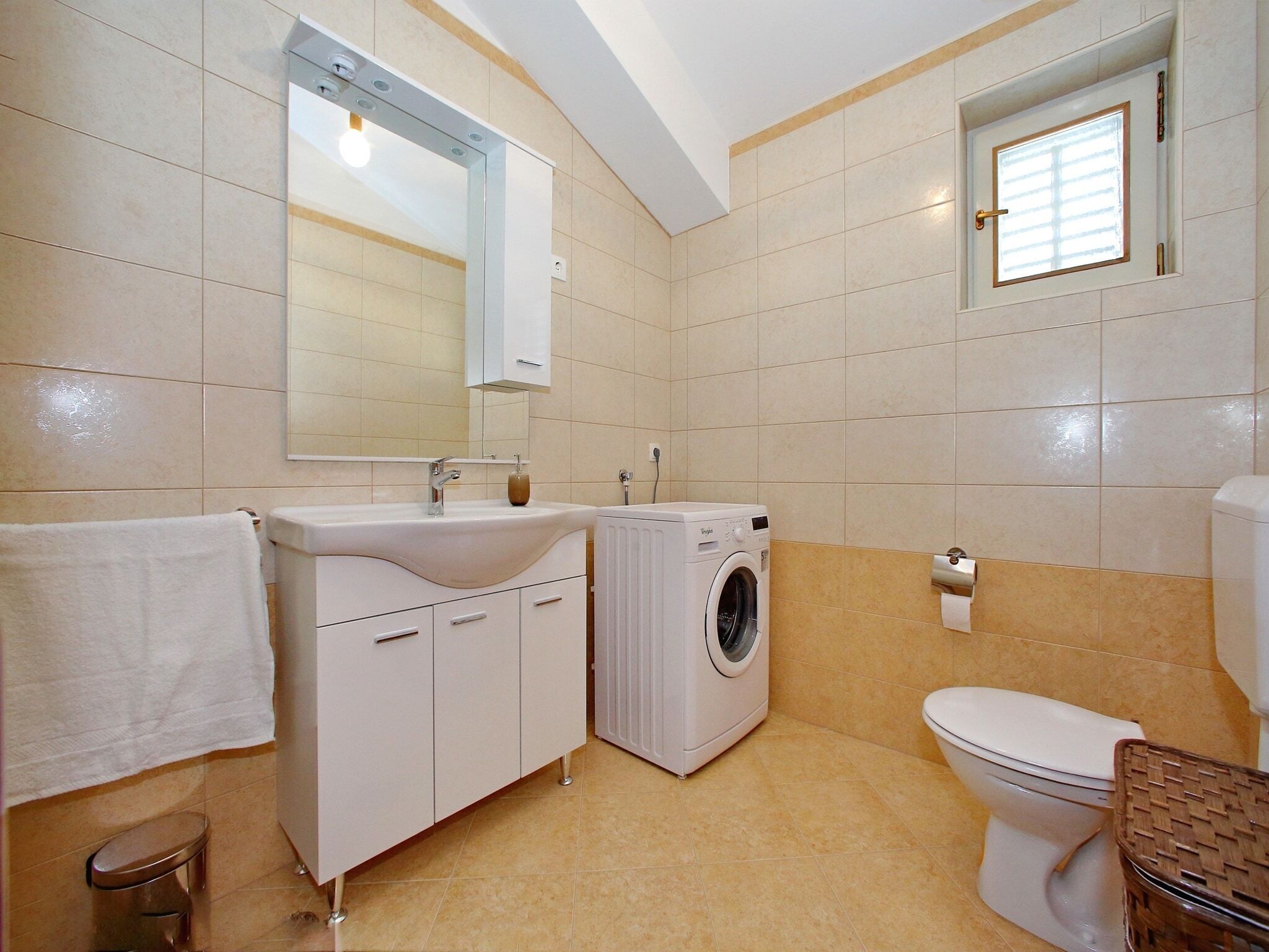 Ein Badezimmer mit Waschbecken, Spiegel, Waschmaschine, Toilette und einem kleinen Fenster.