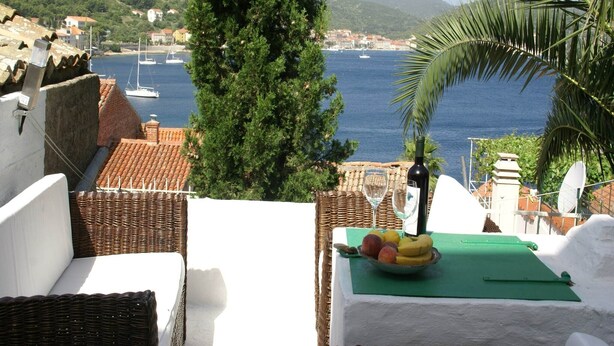 A terrace with a view of the sea, a table with fruit and wine glasses, and a wicker chair. - Coastal apartment in Vis near sea (Vis)