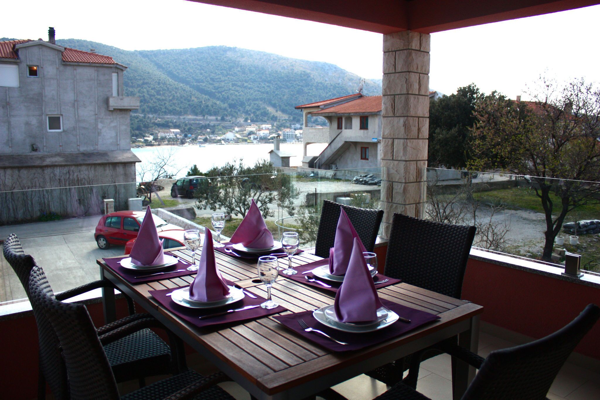A dining table set for four with purple napkins, a view of a body of water, and a mountain in the background.