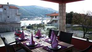 Une table à manger dressée pour quatre personnes, avec des serviettes violettes, donnant sur un plan d’eau et avec une montagne en arrière-plan.