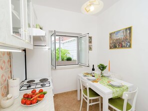 Cocina compacta con estufa a gas, mesa para dos personas y ventana con vistas a la vegetación.