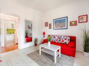 A modern living room with a red sofa, a white coffee table, and a kitchen visible through an open door.