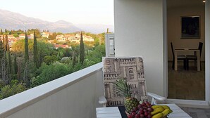 A balcony with a view of a village, a table with a fruit basket, and a chair. - Modern Stay near Cavtat (Močići, Dubrovnik - Konavle Region)