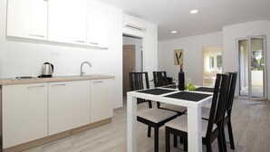 A modern kitchen with white cabinets, a black countertop, and a dining area with a white table and black chairs. - Modern Stay near Cavtat (Močići, Dubrovnik - Konavle Region)