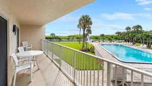 A balcony with a pool, white chairs, and a view of the pool area. - ⛱️ Beach Front Condo🚀🌴👙🚢 (Cocoa Beach)