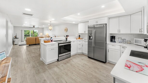 A modern kitchen with white cabinetry, stainless steel appliances, and a wooden floor. - ⛱️ Beach Front Condo🚀🌴👙🚢 (Cocoa Beach)