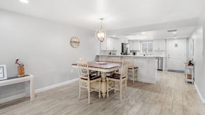 A modern kitchen with white cabinets, a central island, and a dining area with a wooden table and chairs. - ⛱️ Beach Front Condo🚀🌴👙🚢 (Cocoa Beach)