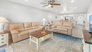 A spacious living room with two beige sofas, a wooden coffee table, and a ceiling fan. - ⛱️ Beach Front Condo🚀🌴👙🚢 (Cocoa Beach)