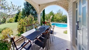 A covered patio with a table and chairs, overlooking a swimming pool and a garden. - Beautiful holiday home with private sauna (Neoric)