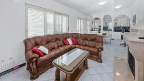A spacious living area with a leather sofa and a glass coffee table, white walls, and a kitchen in the background. - Beautiful holiday home with private sauna (Neoric)
