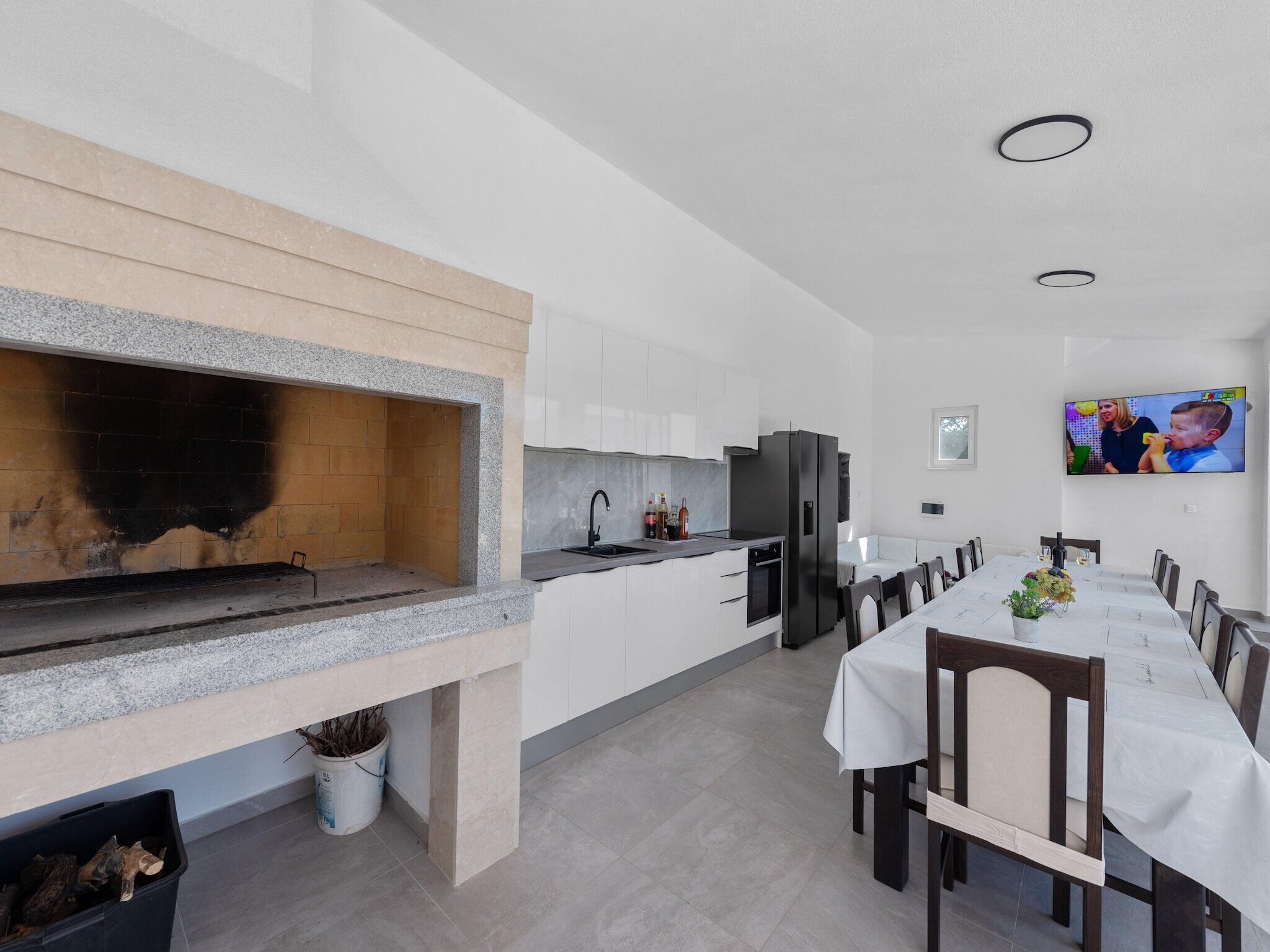 Una cocina moderna con horno empotrado, un comedor con una mesa larga y un televisor montado en la pared.