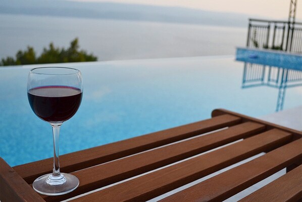 A glass of red wine on a wooden bench overlooking a pool.