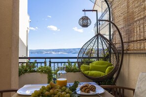 A balcony with a wicker chair, a table with food and drink, and a view of the sea.